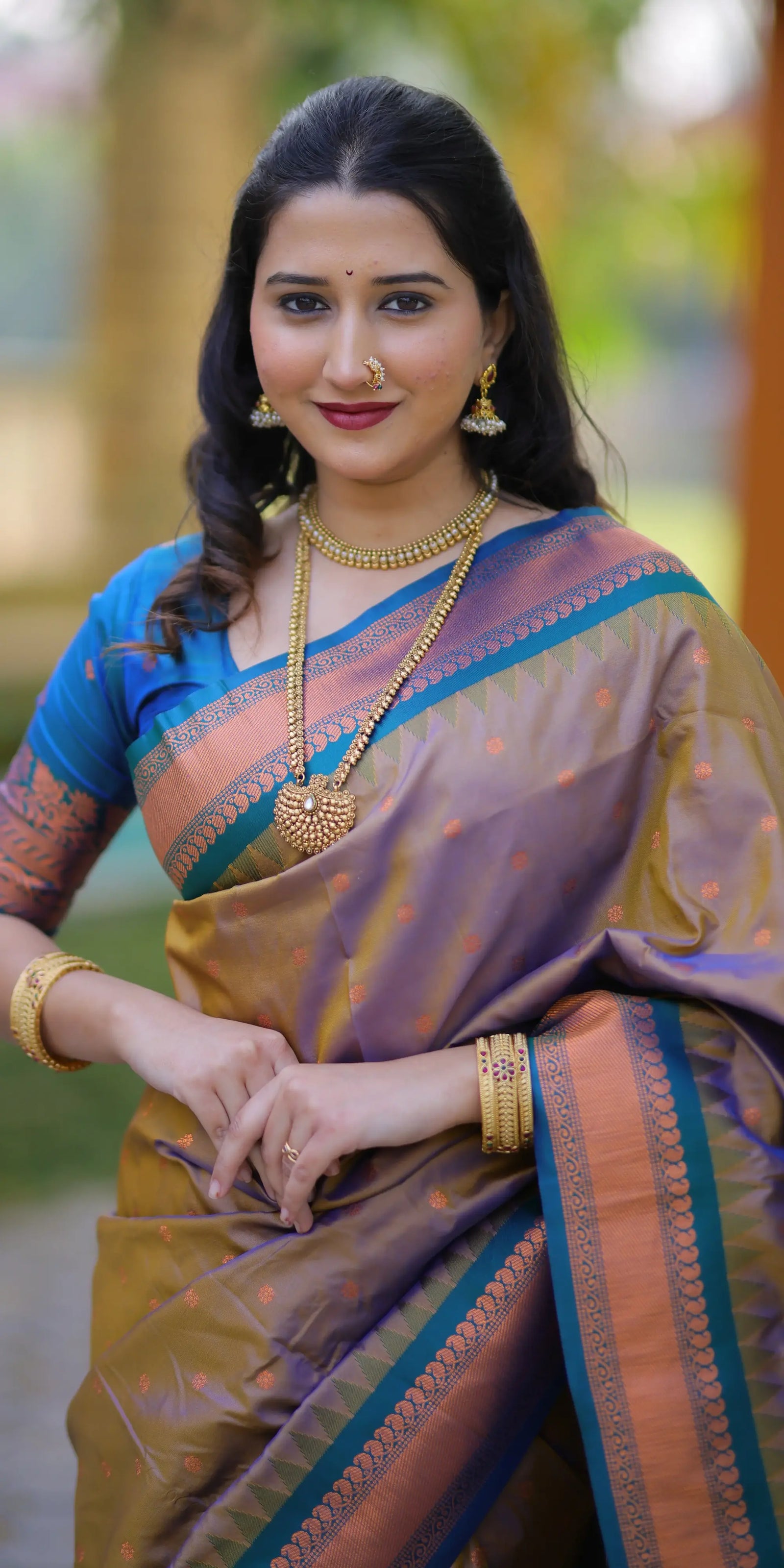 Woman in traditional saree with jewelry against a blurred natural background