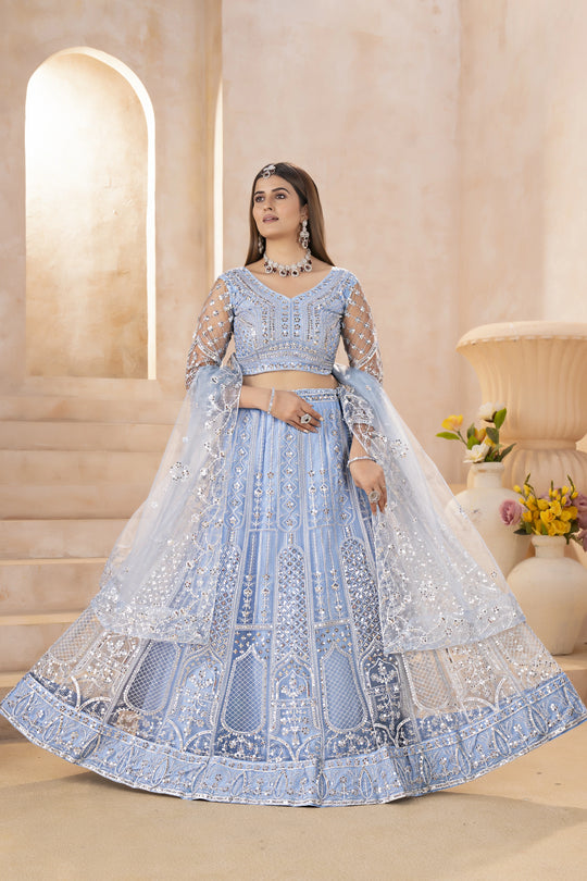 Woman in a light blue embroidered traditional outfit standing in a decorated indoor setting.