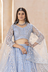 Woman wearing a light blue embroidered lehenga with silver details against a beige background