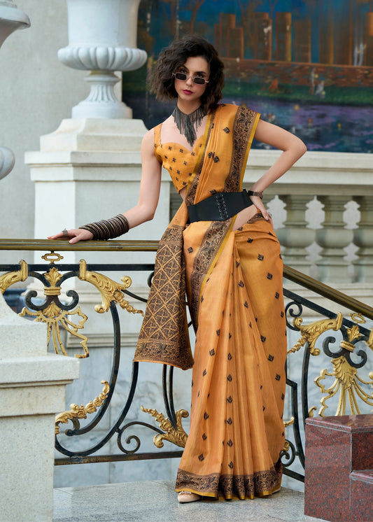 Woman in a mustard yellow saree with black patterns standing on a decorative staircase.