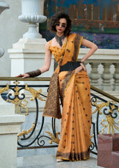 Woman in a mustard yellow saree with black patterns standing on a decorative staircase.
