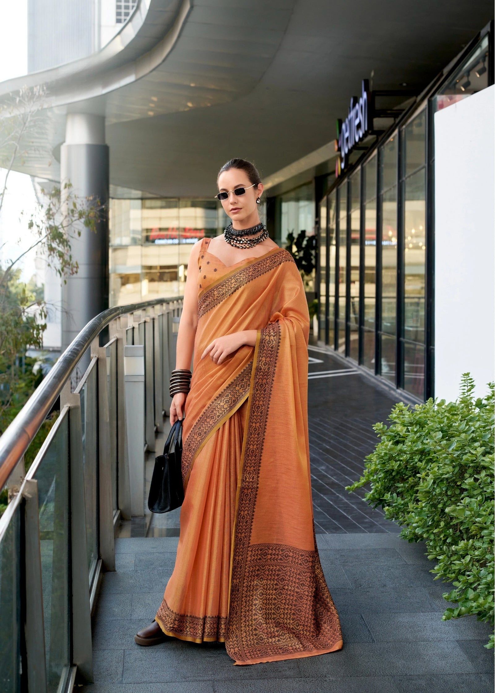 Woman in an orange saree standing on a modern building exterior