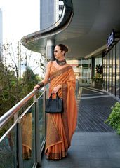 Woman in an orange saree standing on a balcony with modern architecture in the background