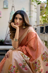 Woman in a peach saree with floral patterns sitting outdoors.