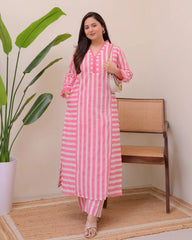Woman wearing a pink and white striped outfit standing in a room with a plant and chair.