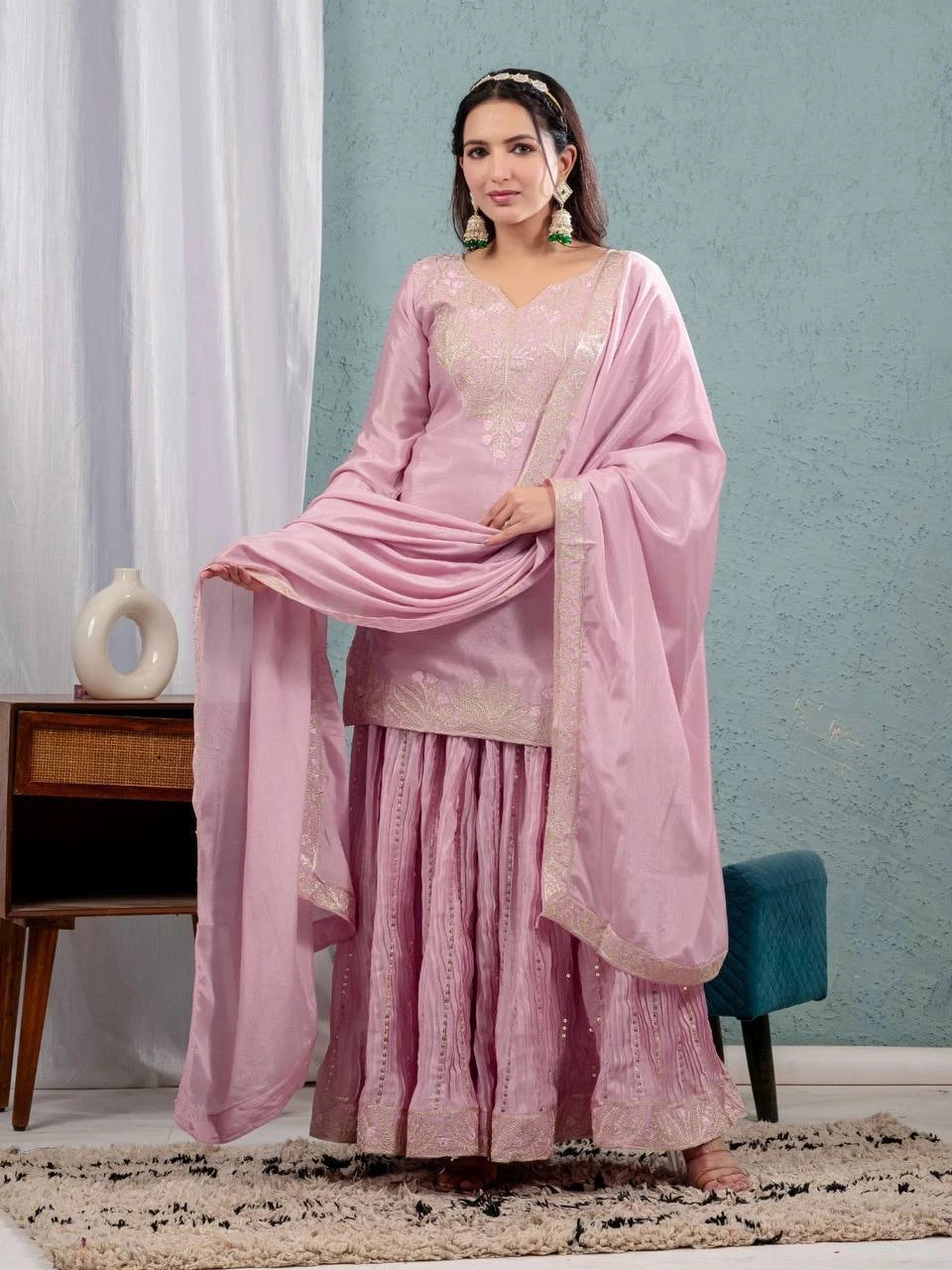 Woman in a pink traditional outfit standing in a room with light blue walls and white curtains.