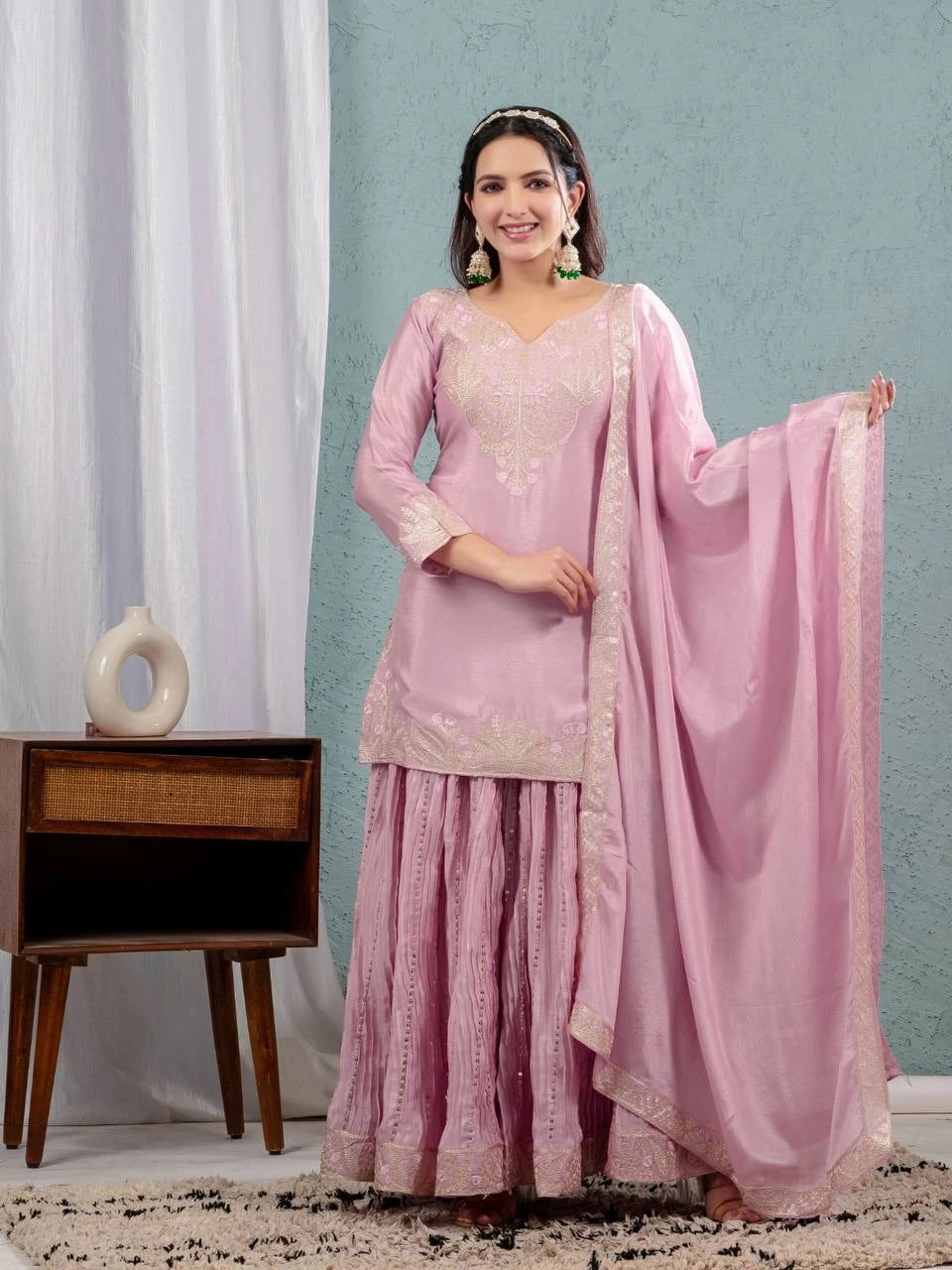 Woman in a pink traditional outfit with a matching dupatta against a light blue wall.