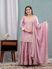 Woman in a pink traditional outfit with a matching dupatta against a light blue wall.