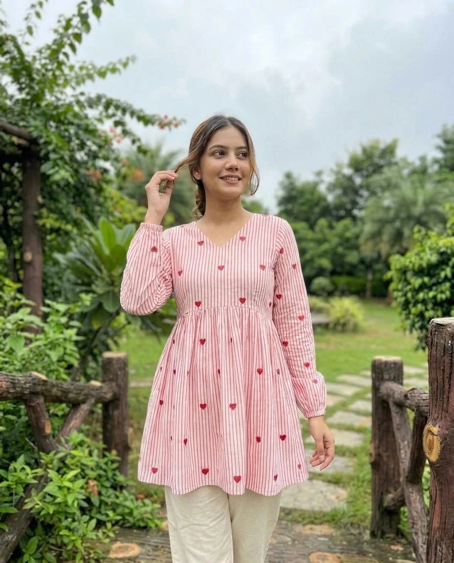 Woman wearing a pink checkered dress with heart patterns in a garden setting