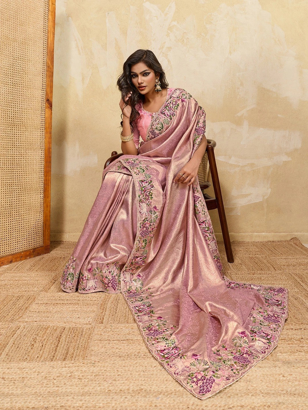 Woman wearing a pink saree with floral patterns sitting on a chair.