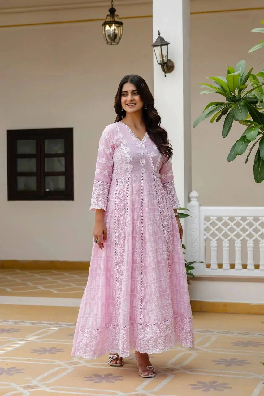 Woman in a pink dress standing in a decorative indoor setting with plants and architectural elements.