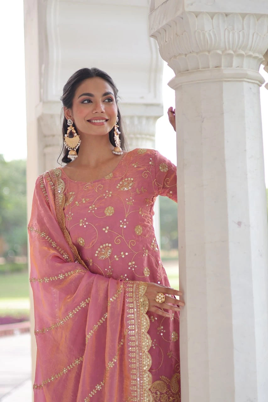 Woman in a pink saree with gold patterns standing against a white architectural background