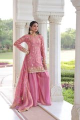 Woman in a pink traditional outfit standing in front of an architectural structure with greenery in the background