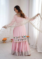 Woman in a pink traditional outfit with intricate designs in a bright room.
