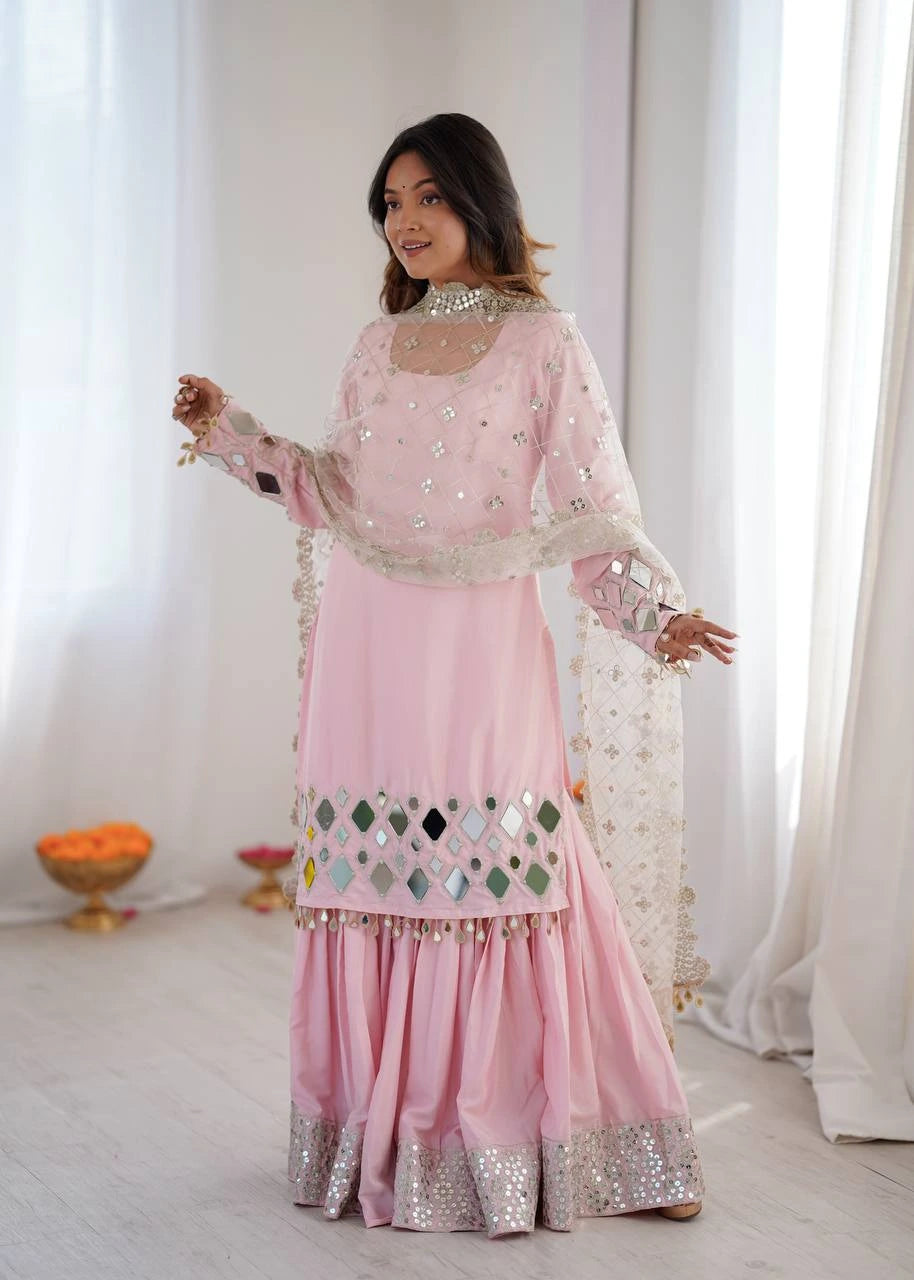Woman wearing a pink traditional outfit with intricate designs in a bright room.