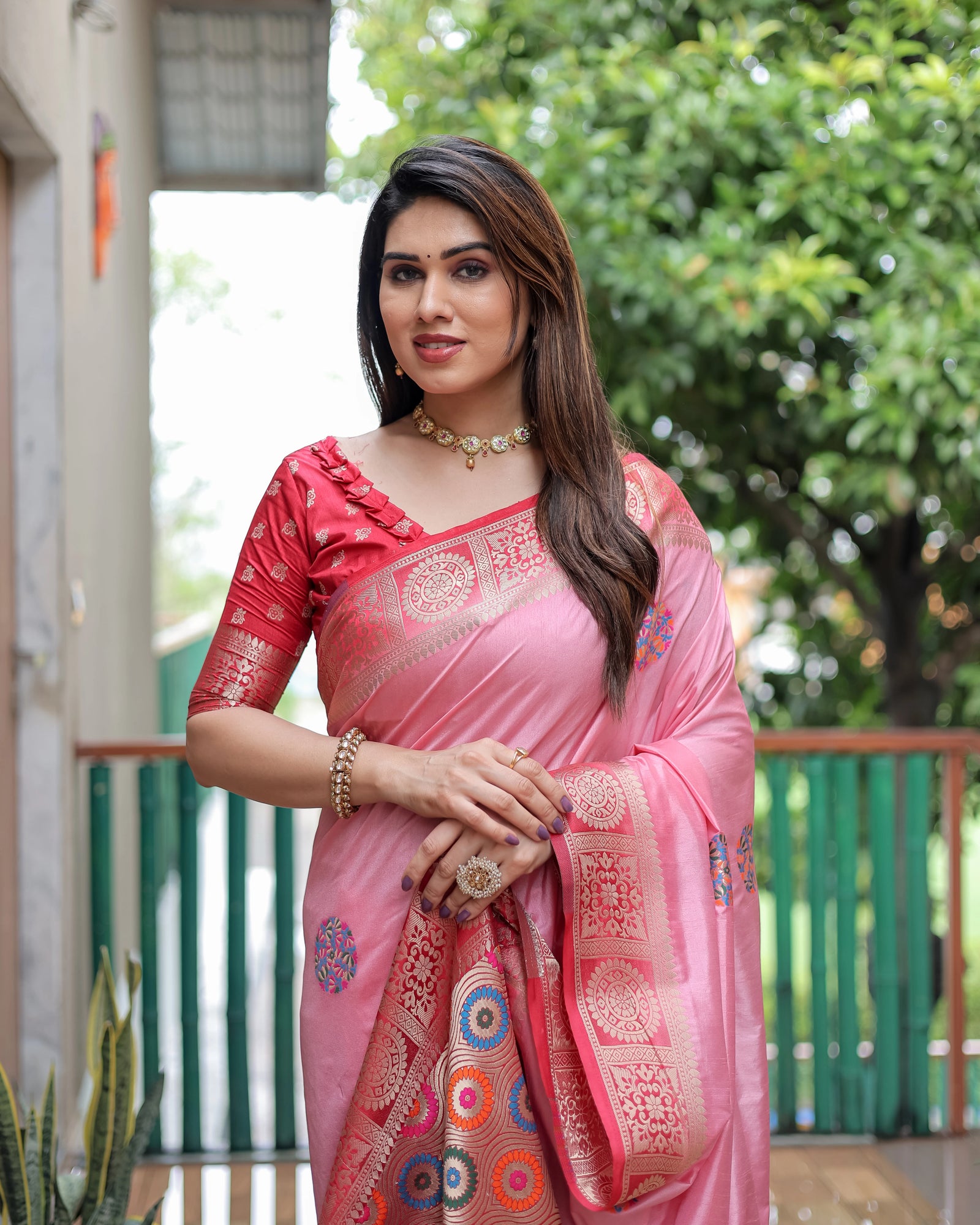 Woman wearing a pink saree with a decorative pattern, standing outdoors.