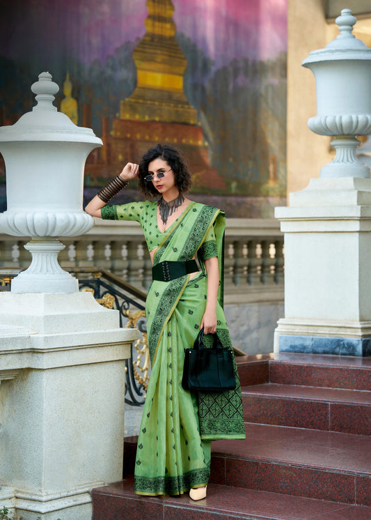 Woman in a green saree standing on steps with classical architecture in the background