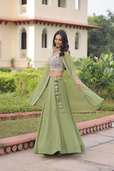 Woman in a green traditional outfit standing outdoors with a building and greenery in the background