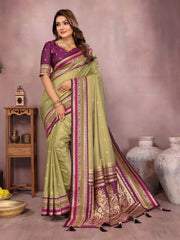 Woman wearing a green and purple saree with a decorative border in a room setting.