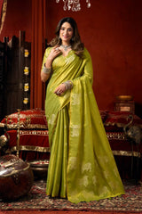 Woman in a green saree standing in a decorated room with red walls and traditional decor.