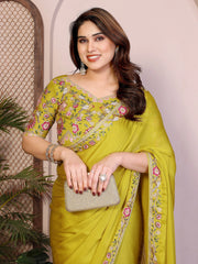 Woman wearing a green saree with floral patterns, holding a clutch, against a neutral background.