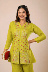 Woman wearing a green embroidered outfit with a red clutch against a beige background