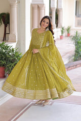 Woman in a green traditional outfit standing in an elegant indoor setting with plants.