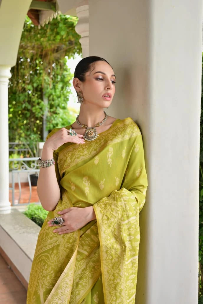 Woman in a green saree standing against a white column with greenery in the background