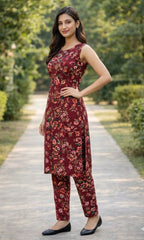 Woman wearing a maroon floral dress standing on a pathway with greenery in the background