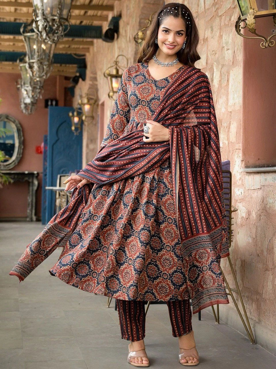 Woman in a traditional patterned outfit standing in an ornate interior setting.
