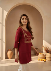 Woman in a red traditional outfit standing in a decorative room with arches and vases.
