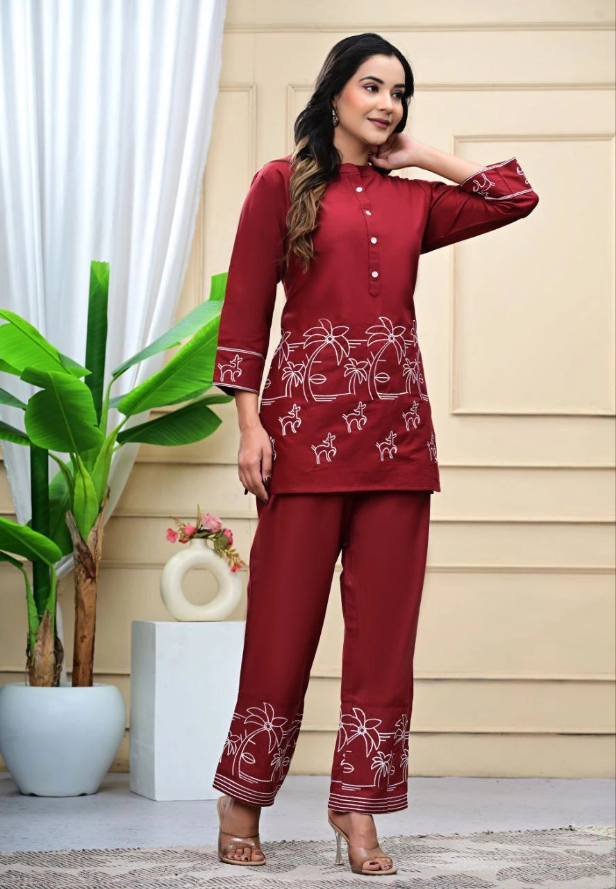 Woman wearing a maroon traditional outfit with white patterns in a home setting.