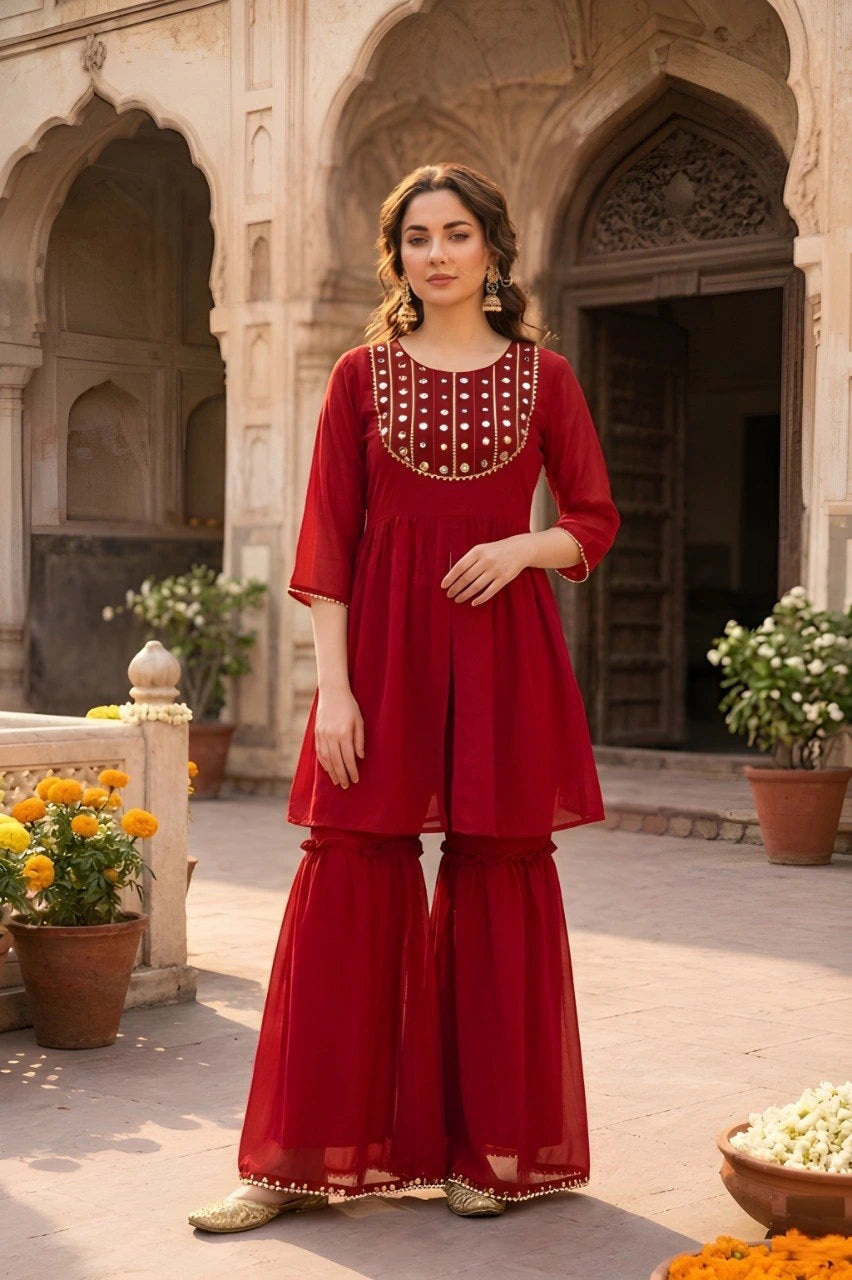 Woman in a red traditional outfit standing in an architectural setting with plants and flowers.