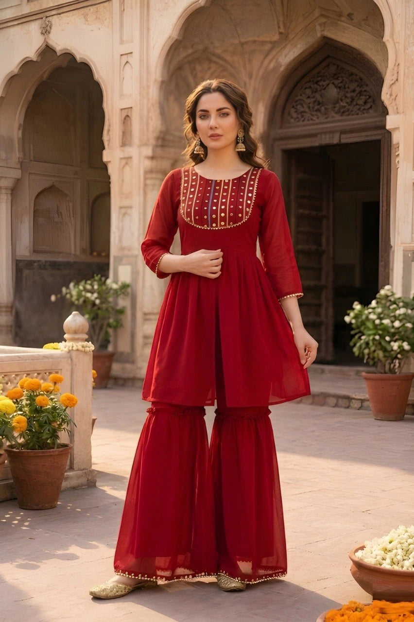 Woman in a red traditional outfit standing in an architectural setting with plants and flowers.