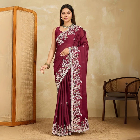 Woman wearing a maroon saree with white floral embroidery in a room setting.