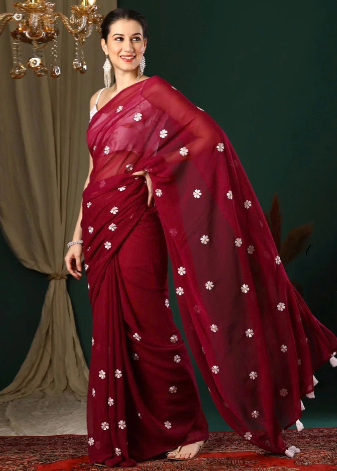 Woman wearing a maroon saree with white patterns in a decorated indoor setting