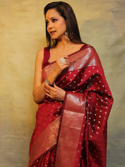 Woman wearing a red saree with gold patterns against a beige background