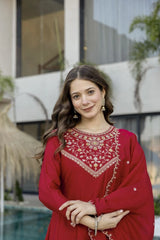 Woman wearing a red traditional outfit with intricate patterns, standing outdoors.