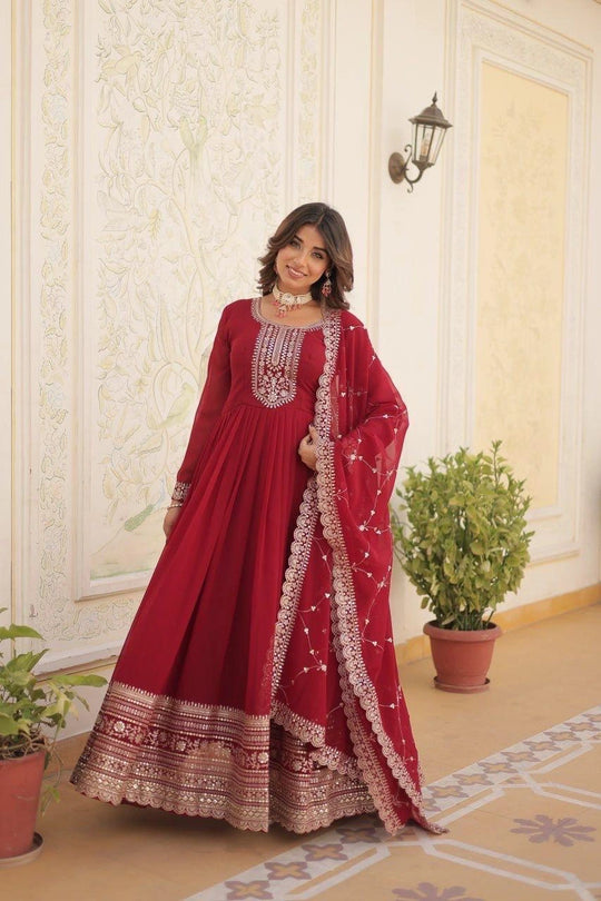 Woman in a red traditional outfit with white embroidery standing in a decorated room.
