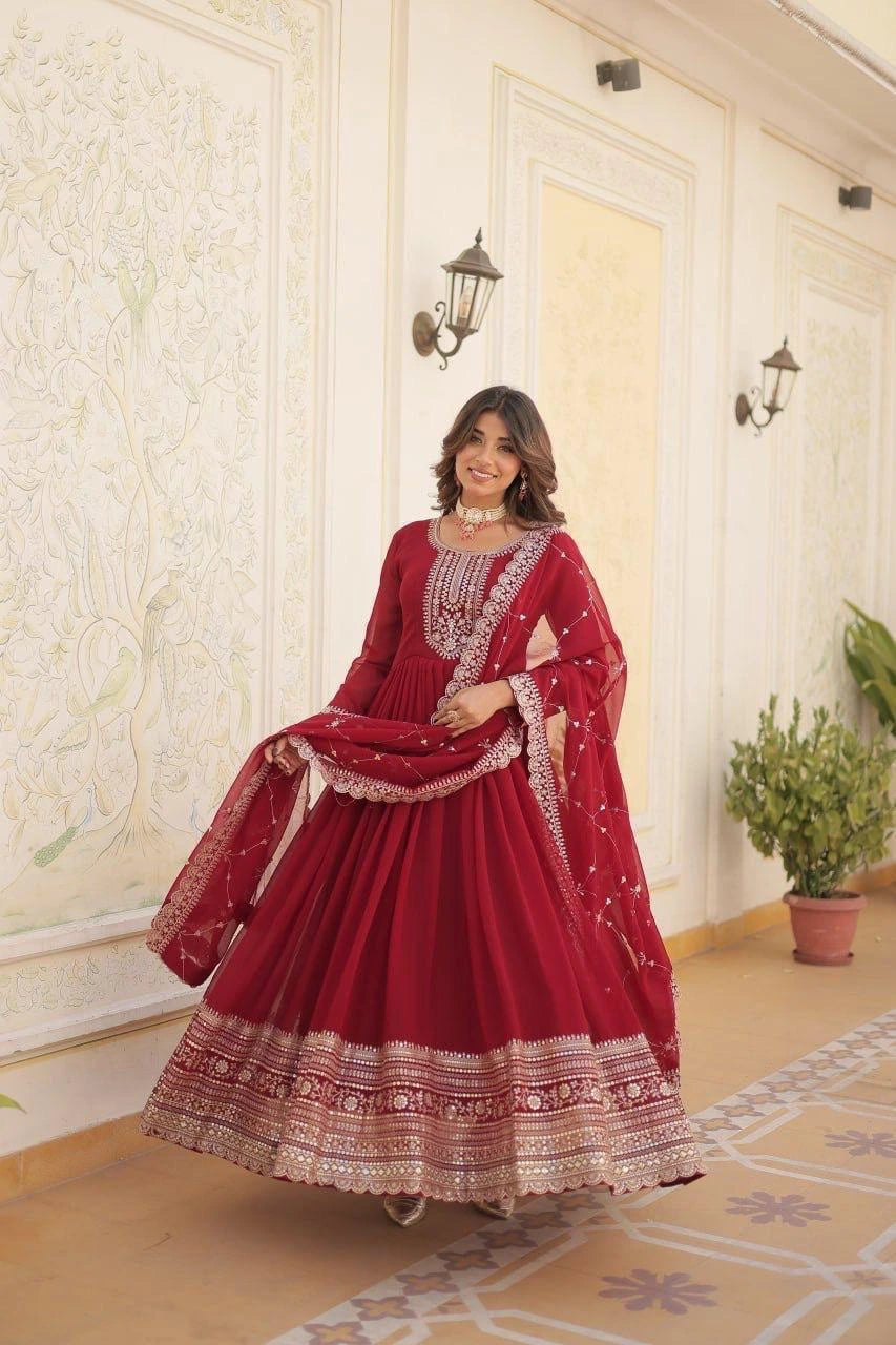 Woman in a red traditional outfit with intricate patterns standing in a decorated room.