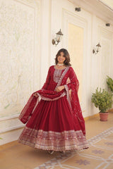 Woman in a red traditional outfit with intricate patterns standing in a decorated room.
