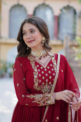 Woman in traditional red outfit with gold embroidery and jewelry, standing outdoors.
