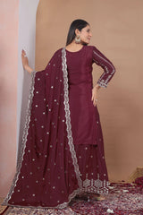 Woman in a maroon traditional outfit with a matching dupatta against a beige wall.
