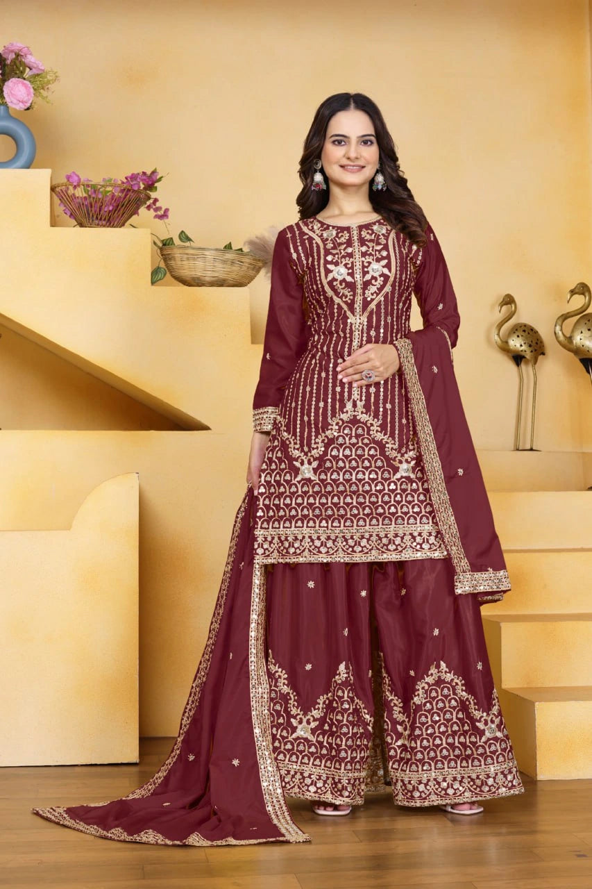 Woman in a maroon embroidered traditional outfit standing in a decorated room.