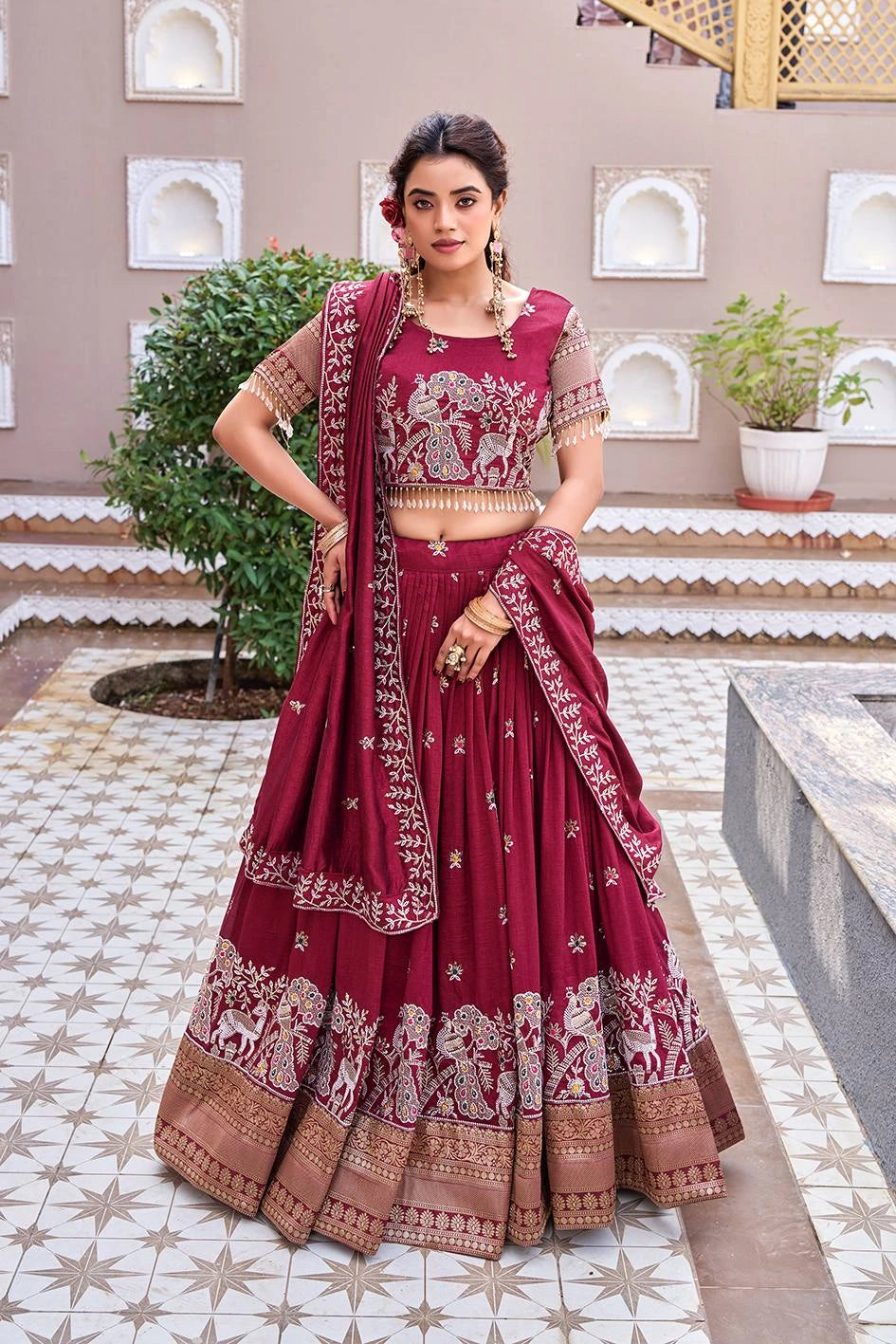 Woman in a traditional maroon and gold saree standing in an outdoor setting.