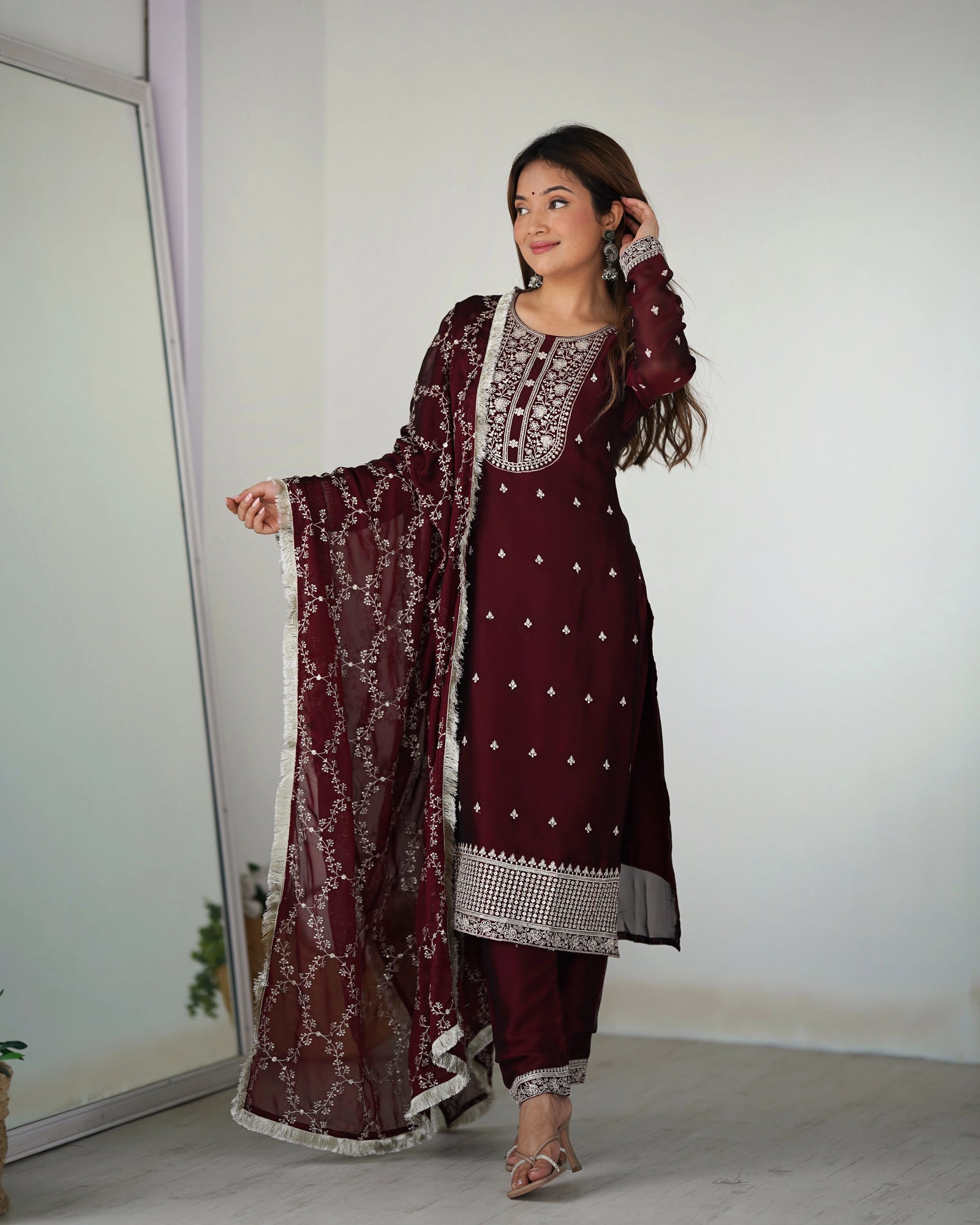 Woman wearing a maroon embroidered outfit with a white background
