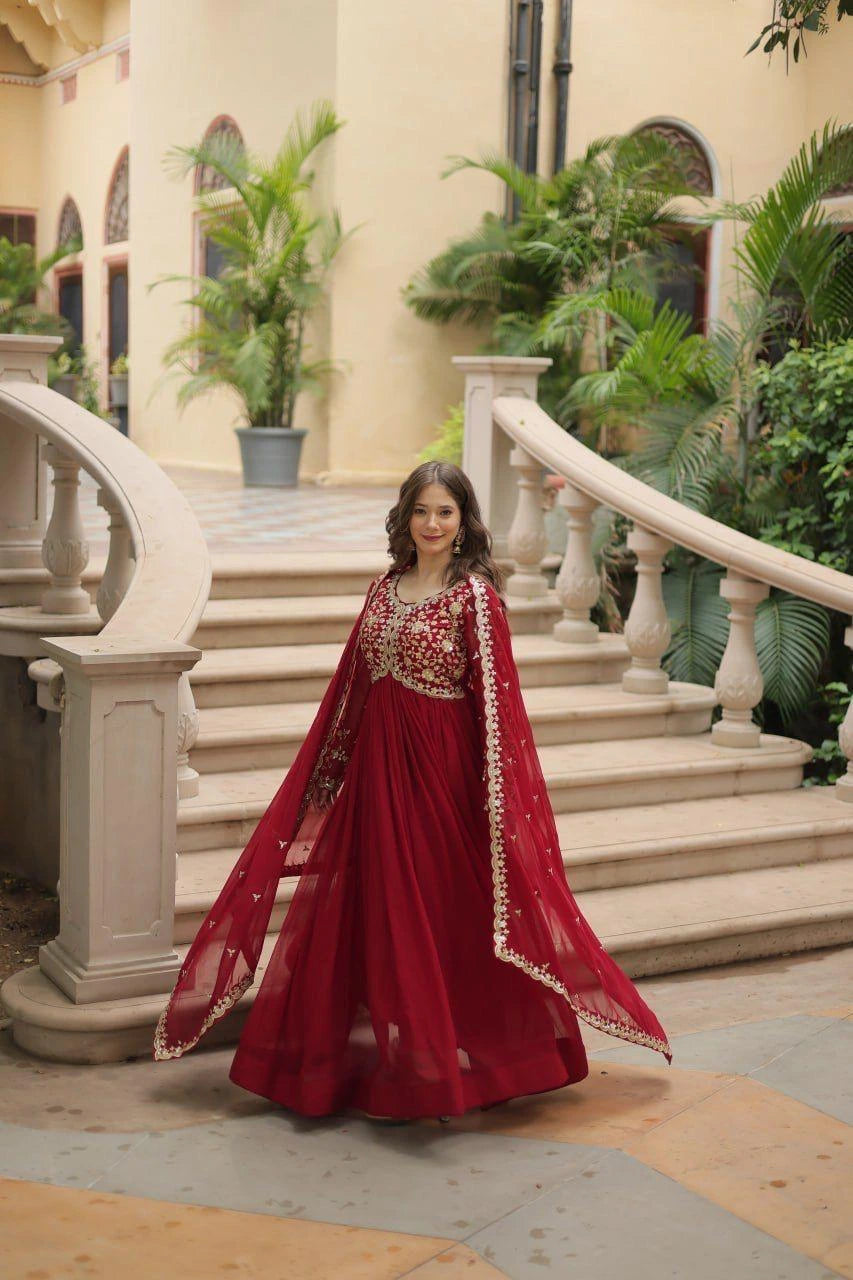 Woman in a red traditional outfit standing on steps with decorative elements and plants in the background