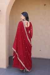 Woman wearing a red saree with gold border against a beige wall.