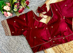 Maroon traditional outfit with gold embroidery on a textured surface with flowers in the background