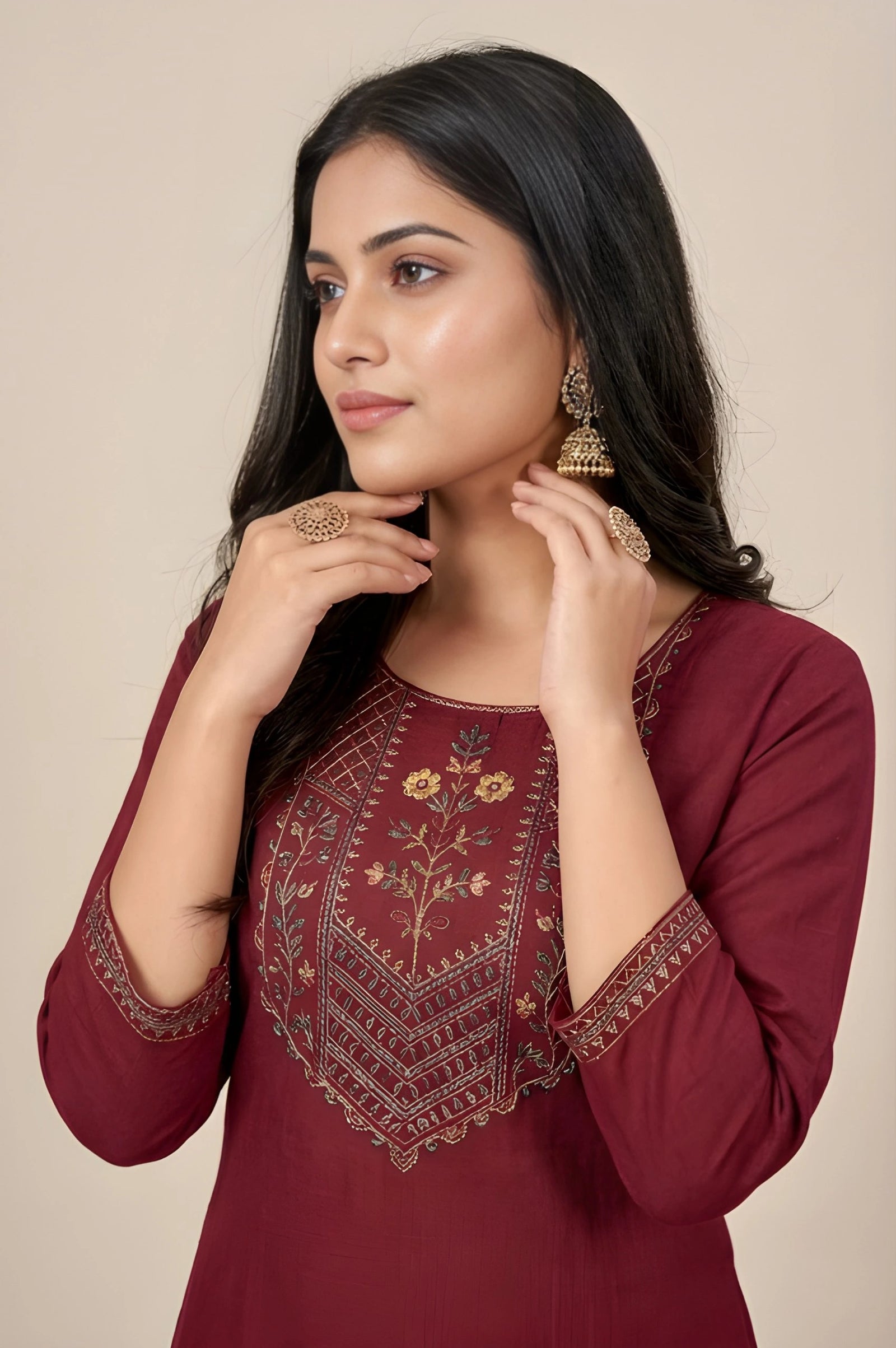 Woman wearing a maroon embroidered top against a beige background